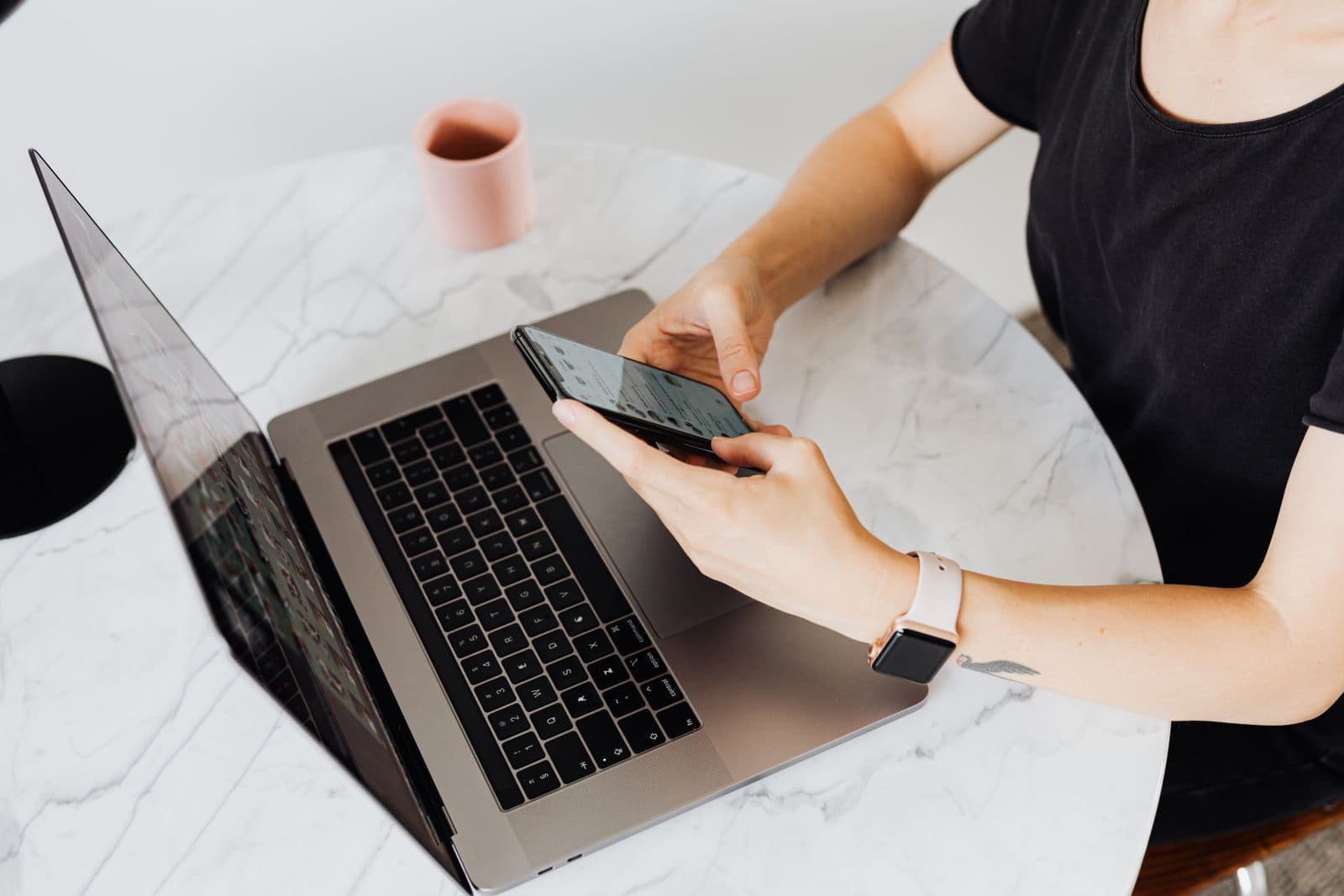 A woman checking her phone beside an open laptop