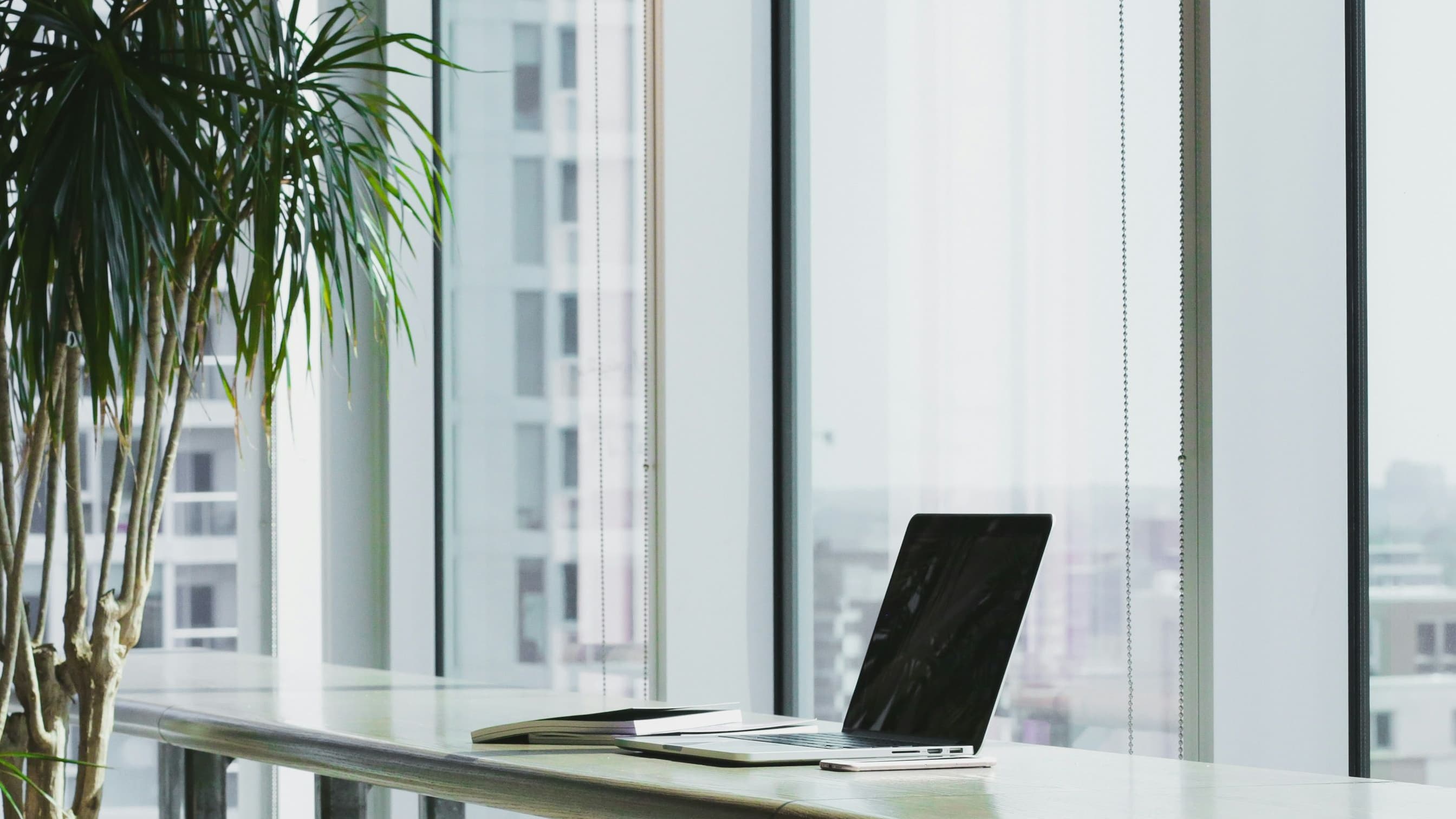A quiet desk with an open laptop and notebook beside a window
